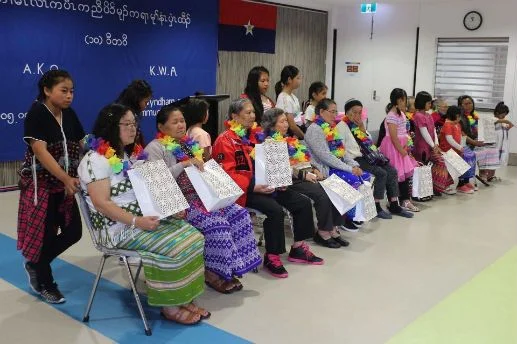 Women seated in a row wearing flower garlands and holding gift bags at the KWO Day celebration in Victoria.