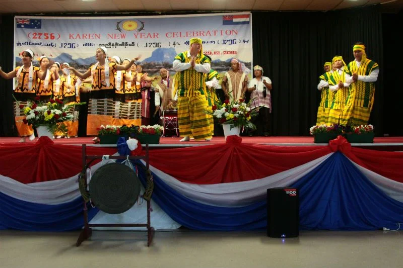 Performers in traditional Karen dress dancing on a stage draped in red, white and blue at the Karen New Year celebration in Perth.