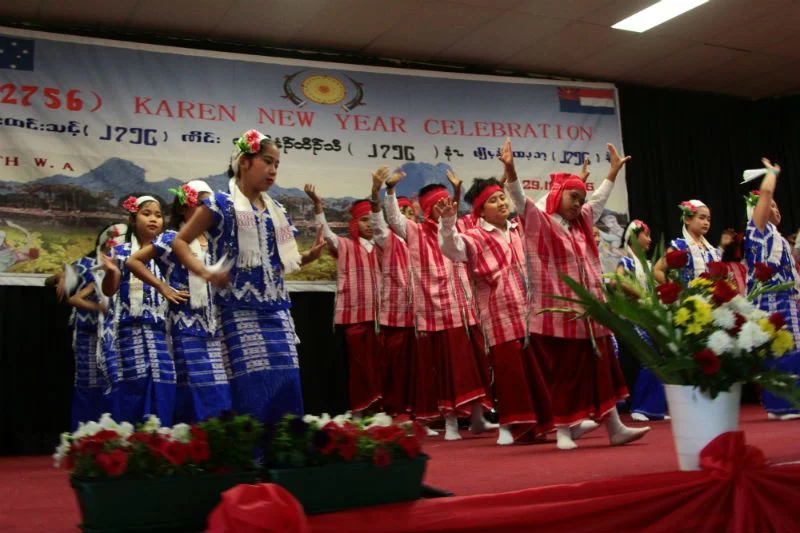 Young dancers in red and blue traditional Karen dress performing the Don dance on stage beneath a Karen New Year celebration banner.