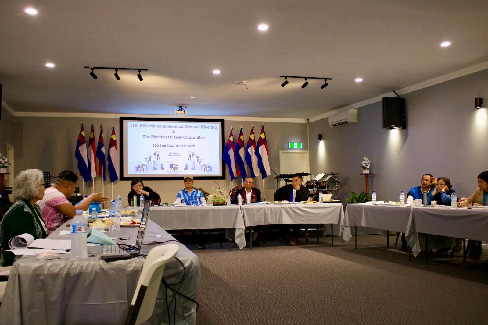 Representatives seated at long tables facing a screen and a row of Karen flags during the 11th National Biennial General Meeting.
